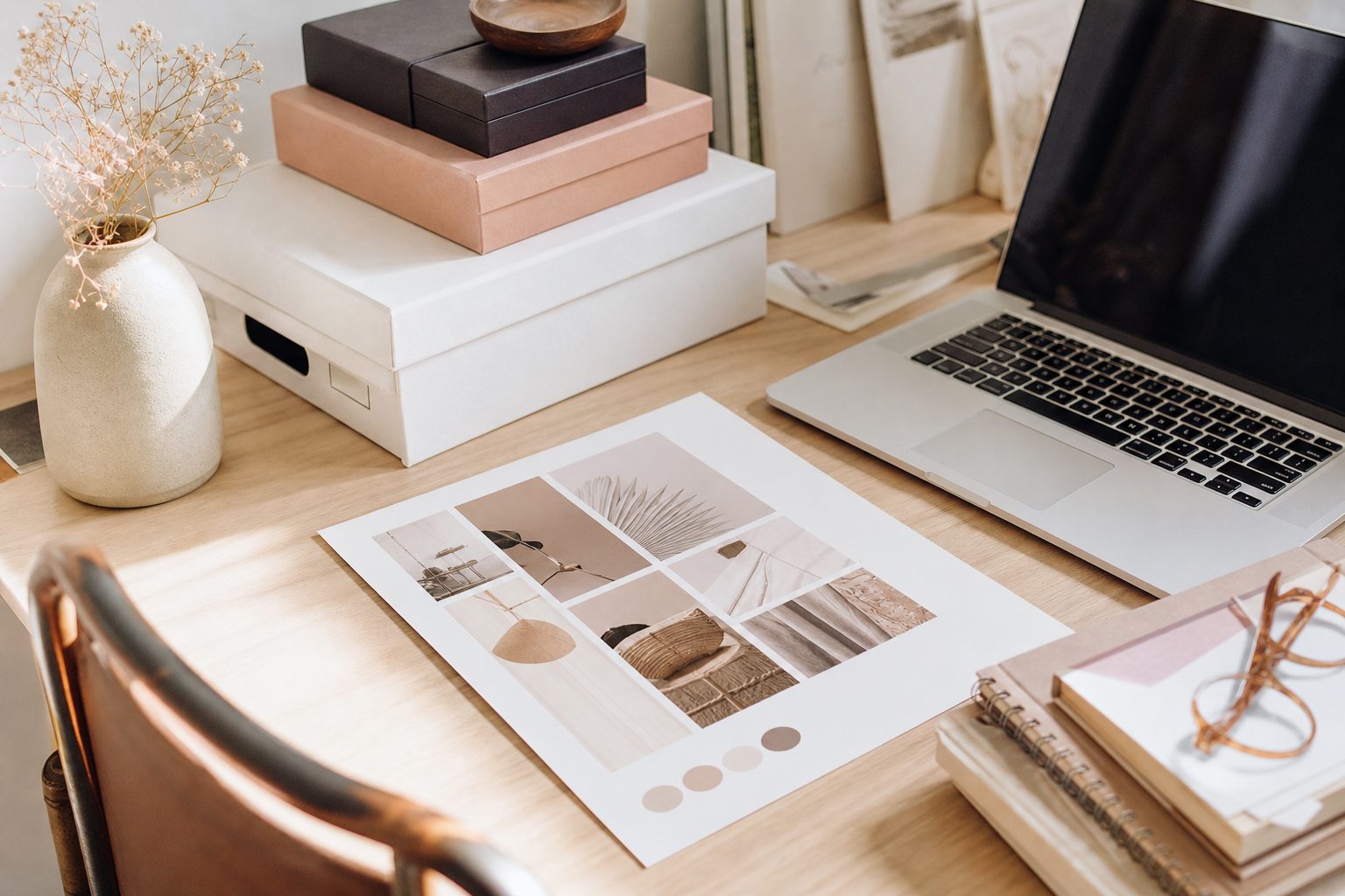Bright studio desk with a printed menu, archival boxes and an open laptop in daylight